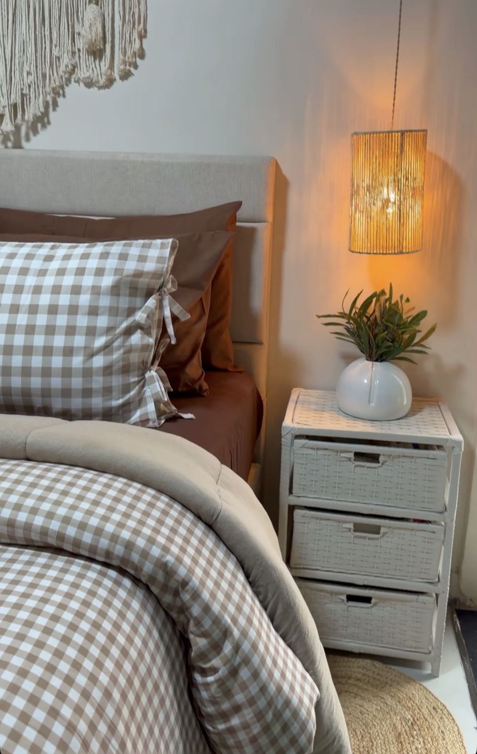 Cama com roupa de cama xadrez e criado-mudo de vime